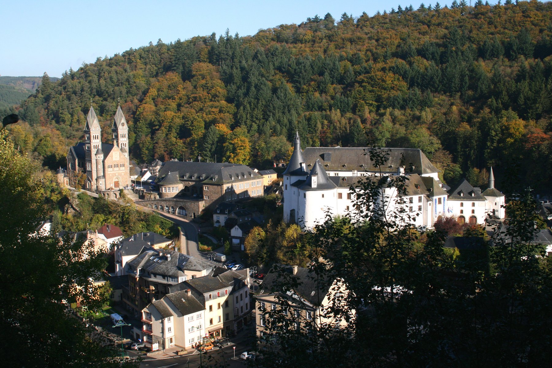 View over Clervaux, with the church and the castle visible among the surrounding hills covered in autumn forest.